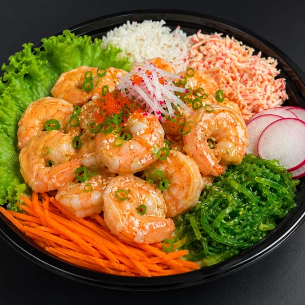 Shrimp poke bowl with rice, crab salad, seaweed, carrots, lettuce, radishes, and roe.