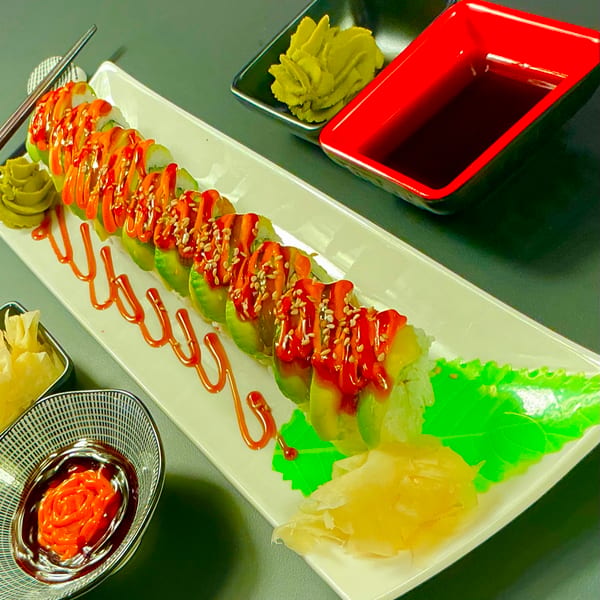 Sushi roll with avocado, red sauce, sesame seeds, wasabi, and soy sauce on a white plate.